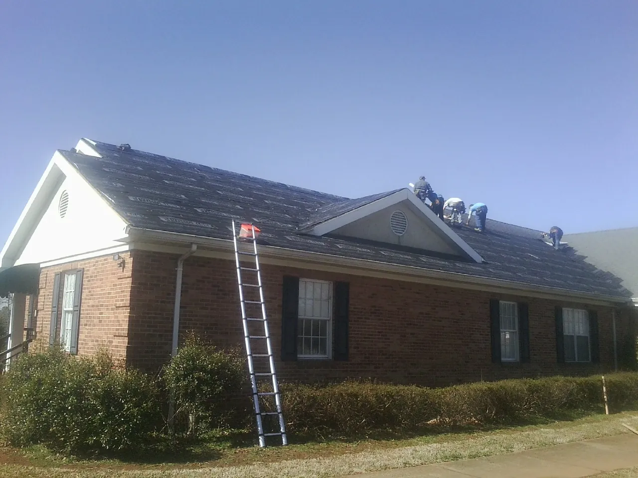 Crew tearing shingles off a brick ranch roof with a ladder set — Emergency Roof Repair work by our crew in Shelburne Falls
