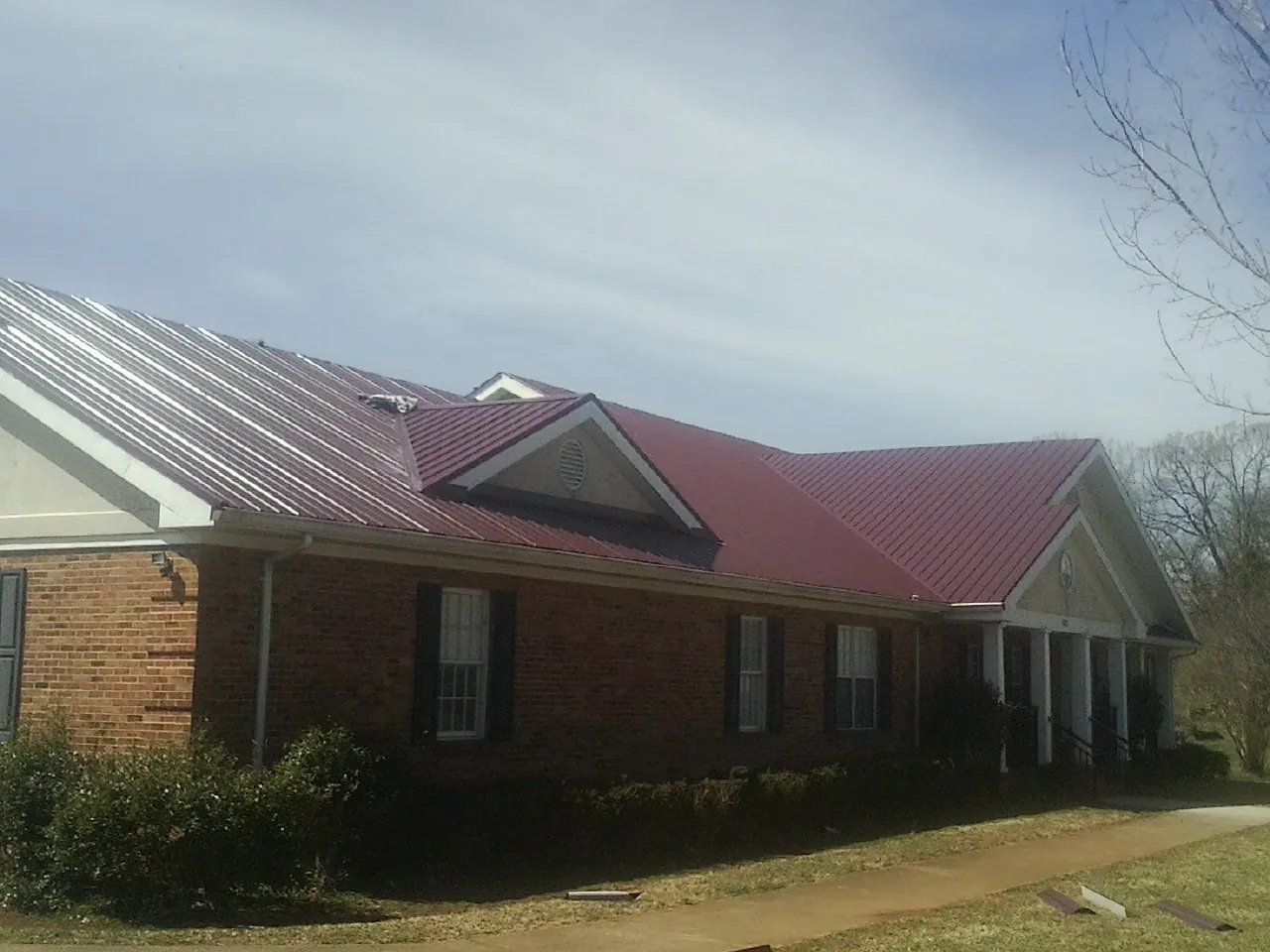 Red metal roof with gabled entries on a long brick building, from a Hail Damage Roof Repair job in Shelburne Falls