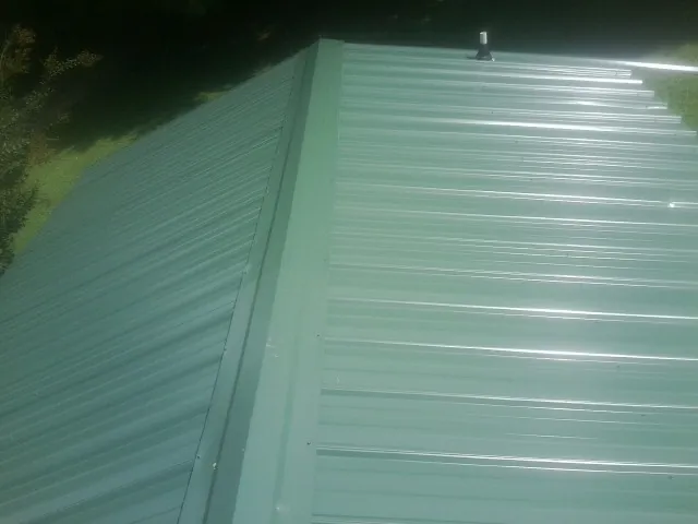 New green metal panels meeting at the ridge of a roof — Flat Roof Repair work by our crew in Shelburne Falls