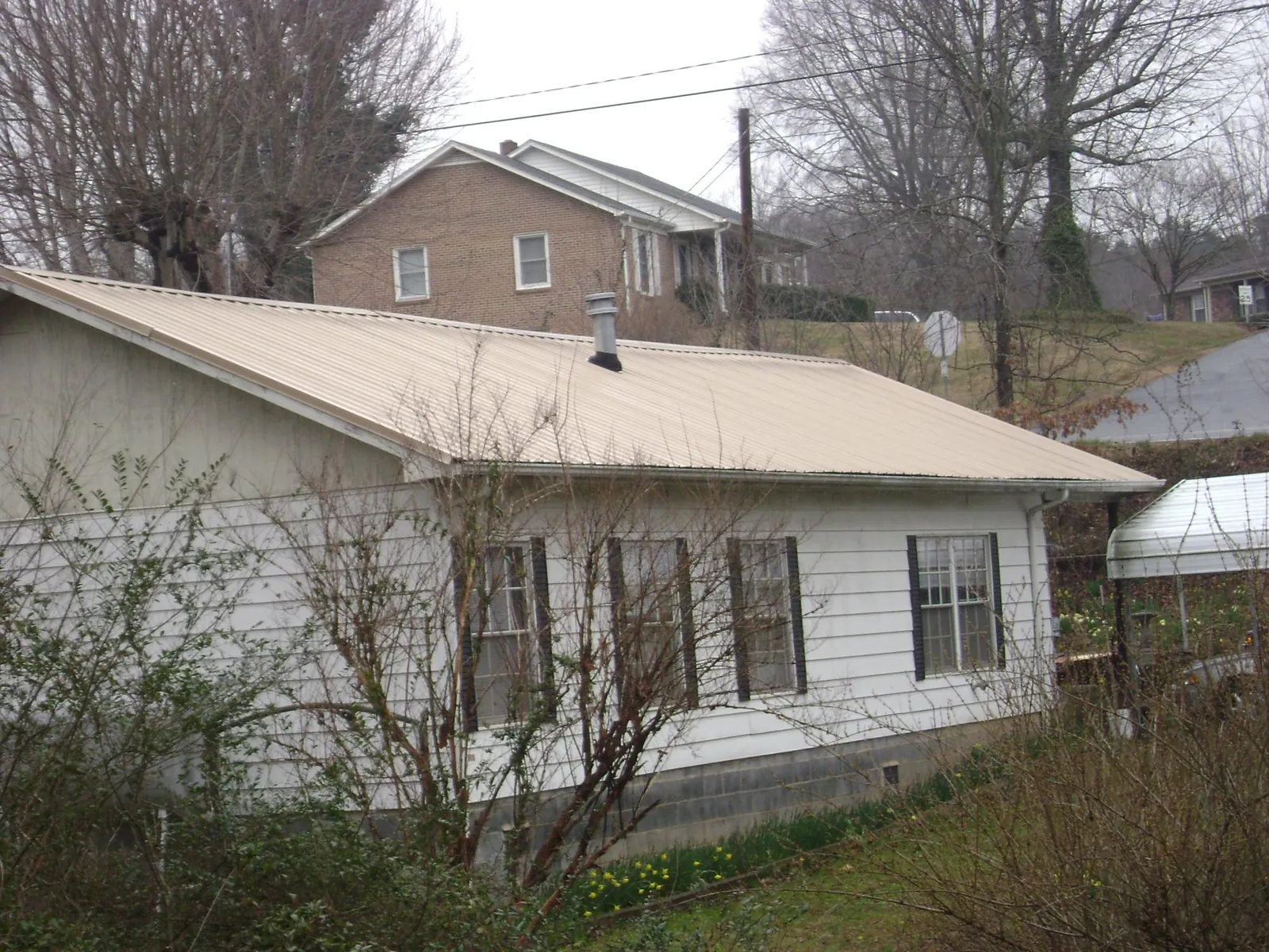 Tan metal roof on a white sided house set into a hillside — Commercial Roofing by Roofing Brothers in Shelburne Falls