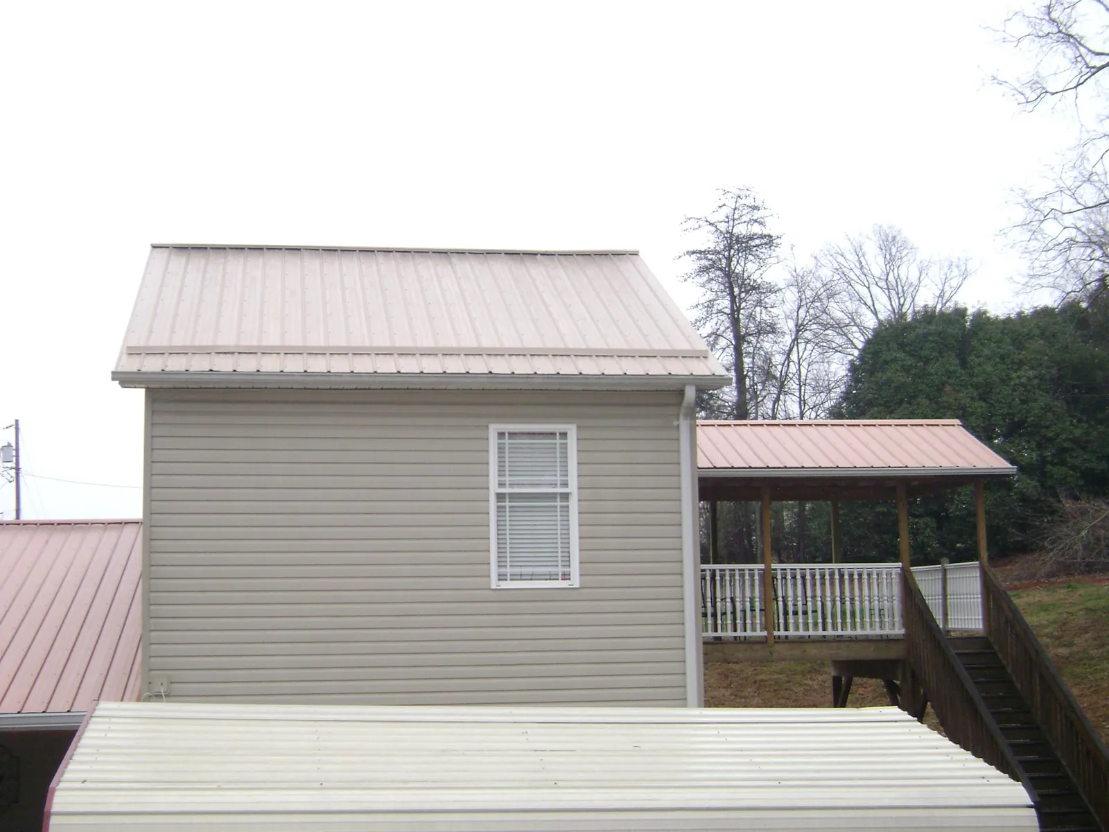 Tan metal roofs on a two story addition and attached porch, from a Roof Replacement job in Shelburne Falls