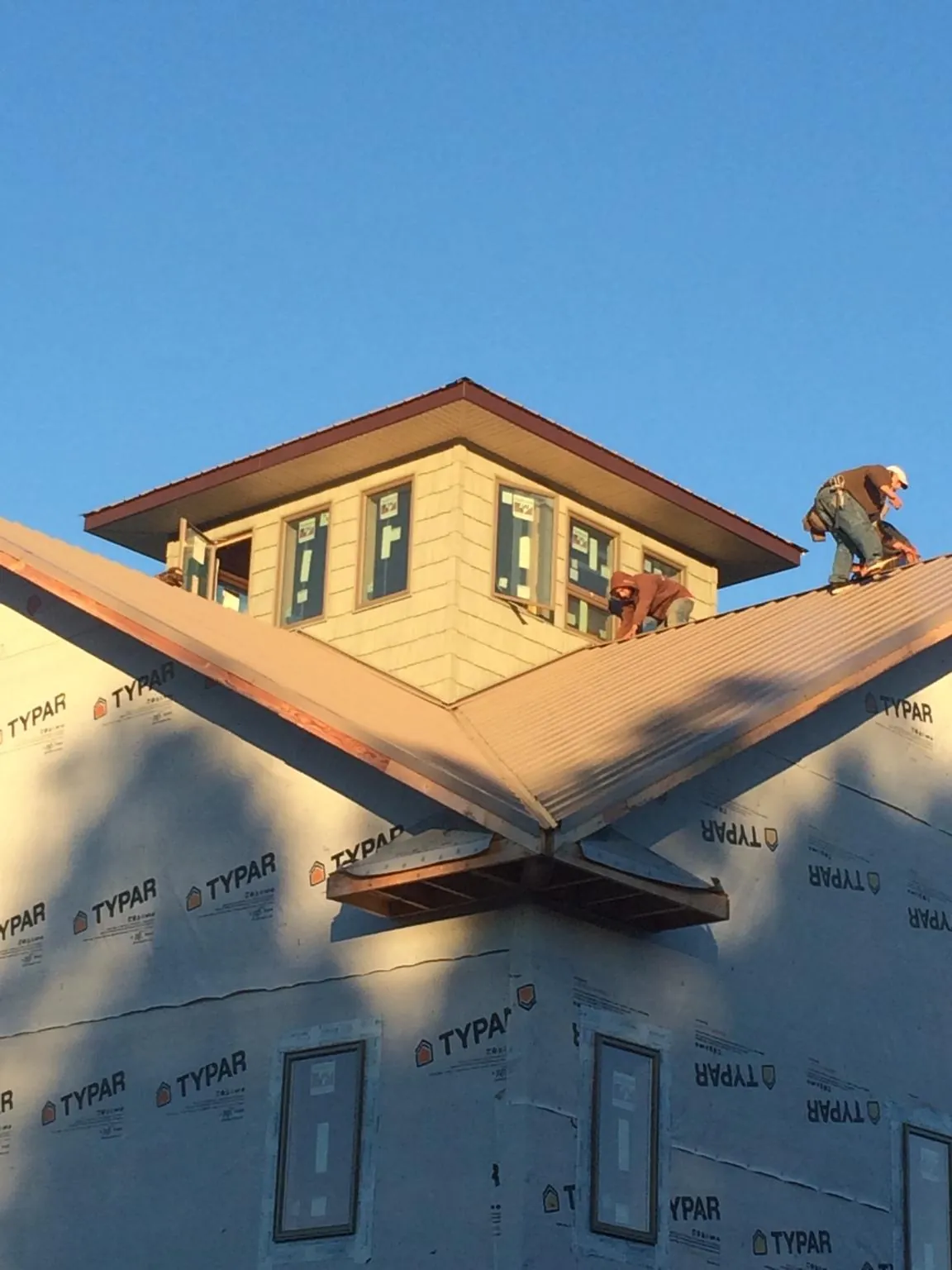 Roofers working around a rooftop cupola on a new metal roof at sunset — Roof Waterproofing in Shelburne Falls by Roofing Brothers